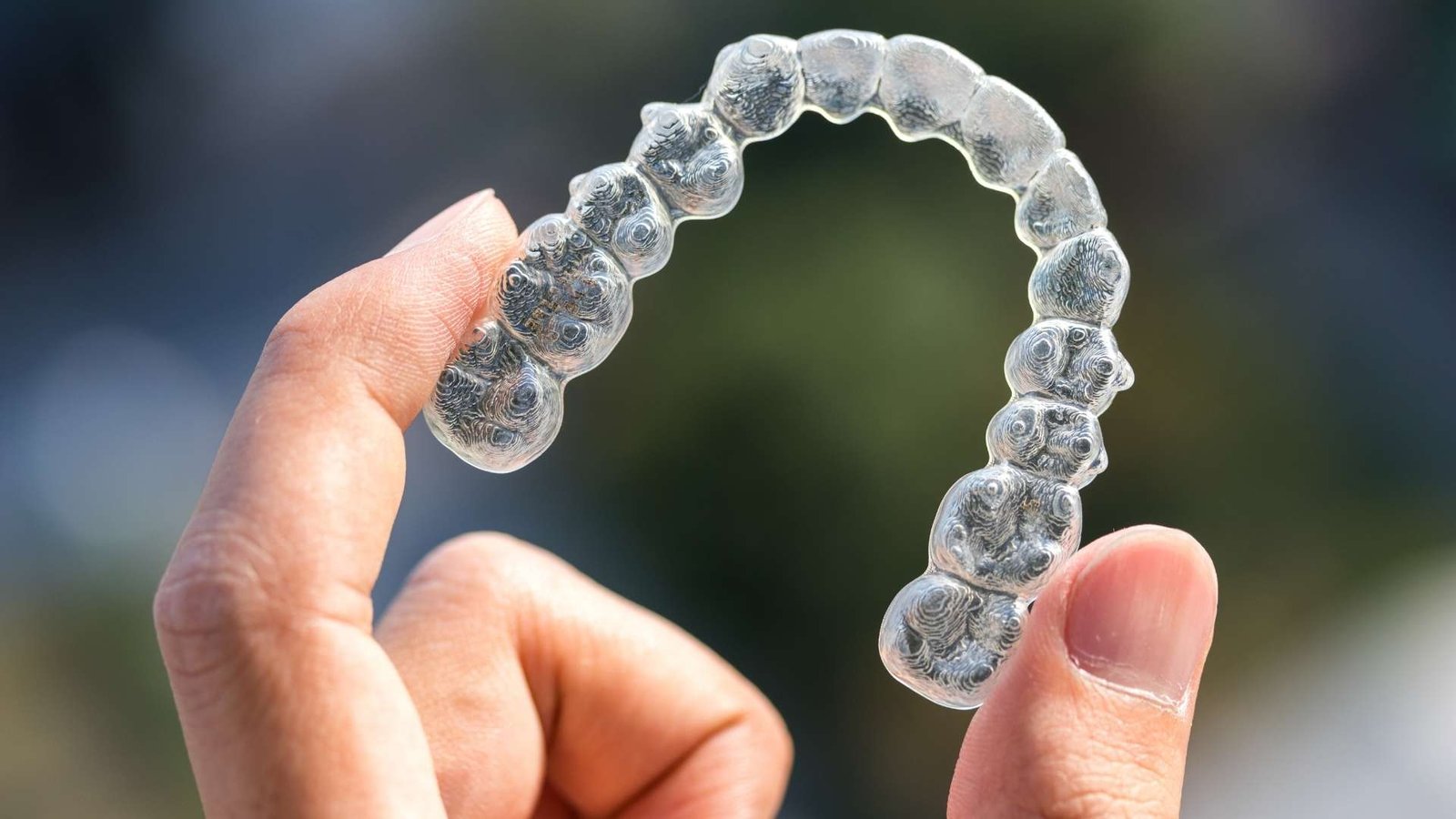 A hand holding a tray of clear aligners