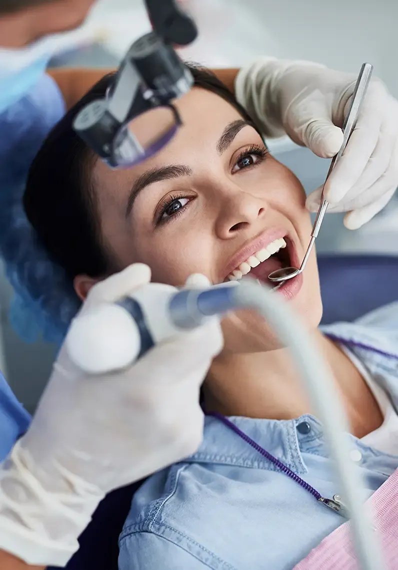 Patient smiling during dental examination with dentist and tools.