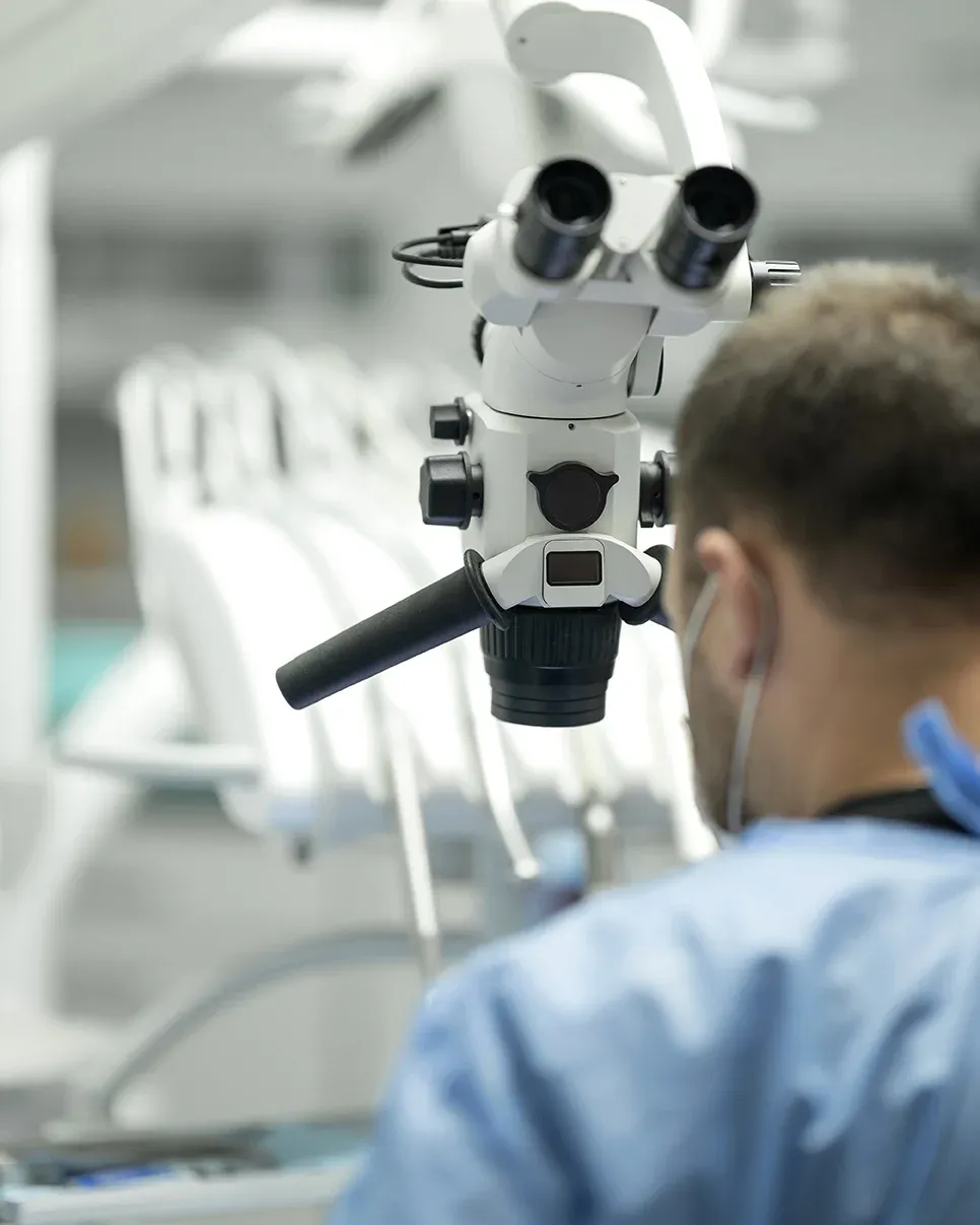 Surgeon using a microscope in a clinical setting.
